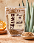 A clear stand-up pouch of Gran Mitla Sal de Gusano (Agave Worm Salt with Chili) is displayed on a rustic wooden surface. The packaging features a cream-colored label with black text and graphics.