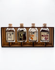 Four small glass bottles of spices displayed in a wooden tray. The bottles are labeled Gran Milla, Chaplin Milla, Habanero, and Jamaica, with cork stoppers and clear glass bodies showing the spices inside.