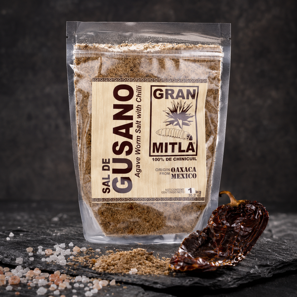 Gran Mitla Sal de Gusano 1kg bag with dried chili peppers and sea salt on dark slate — bold spicy worm salt from Oaxaca
