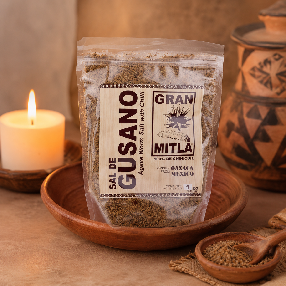 Gran Mitla Sal de Gusano 1kg bag on a clay plate with candle and Oaxacan pottery — handcrafted agave worm salt
