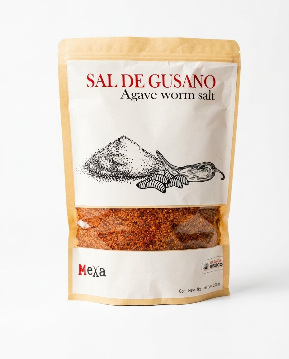 A stand-up pouch of Mexa brand Sal de Gusano (Agave Worm Salt) on a clean white background. The packaging features a kraft paper border, a white center label with red and black text, and a clear window showing the reddish-brown salt inside.